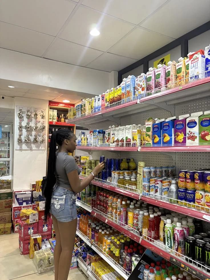 Cliente choisissant une boisson dans les rayons d'une supérette, un stock varié qu'une application de gestion permet de suivre produit par produit